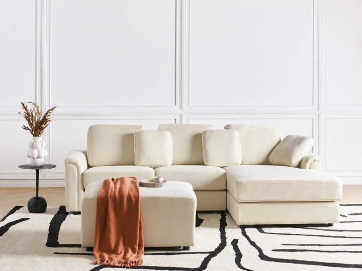 Beige sectional sofa in a living room with a white wall and black and white rug.
