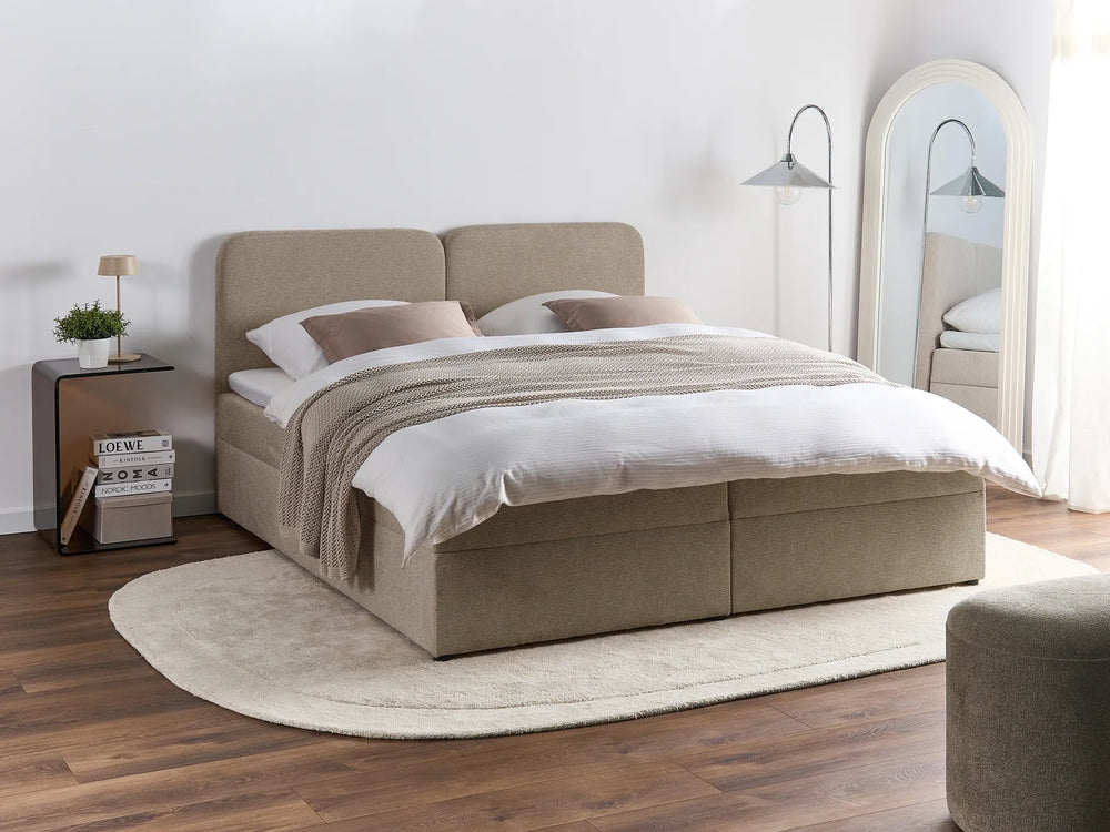 Beige upholstered bed in a bedroom setting with wooden flooring and a mirror.