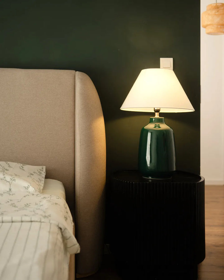 Green lamp on a nightstand next to a bed with beige headboard