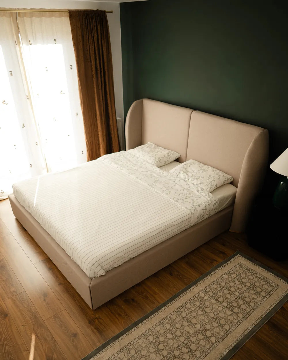 Beige bed with white bedding in a room with a window and dark green wall.