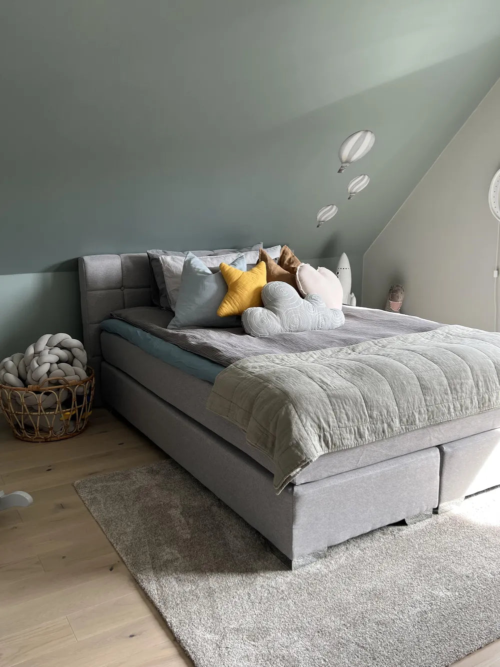 Gray upholstered bed with colorful pillows against a light green wall.