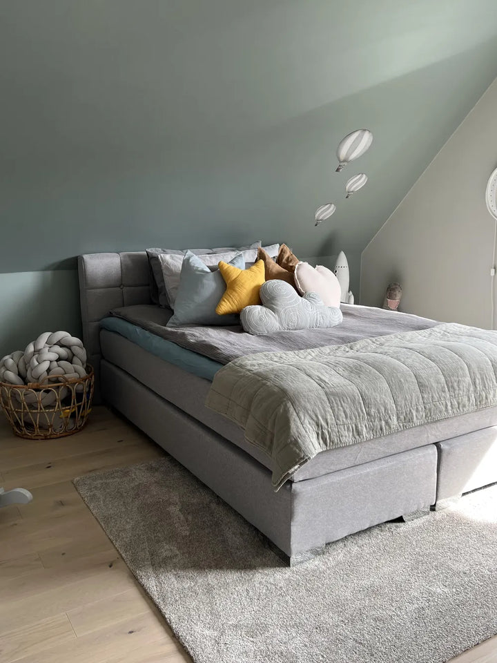 Gray upholstered bed with colorful pillows against a light green wall.