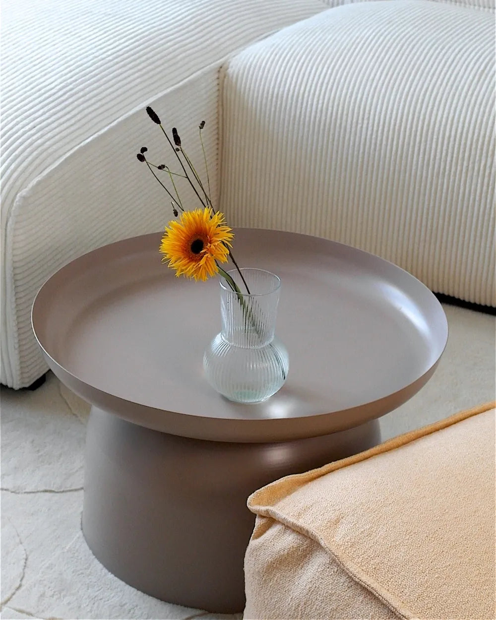Round coffee table with a vase of yellow flowers on a light-colored floor.