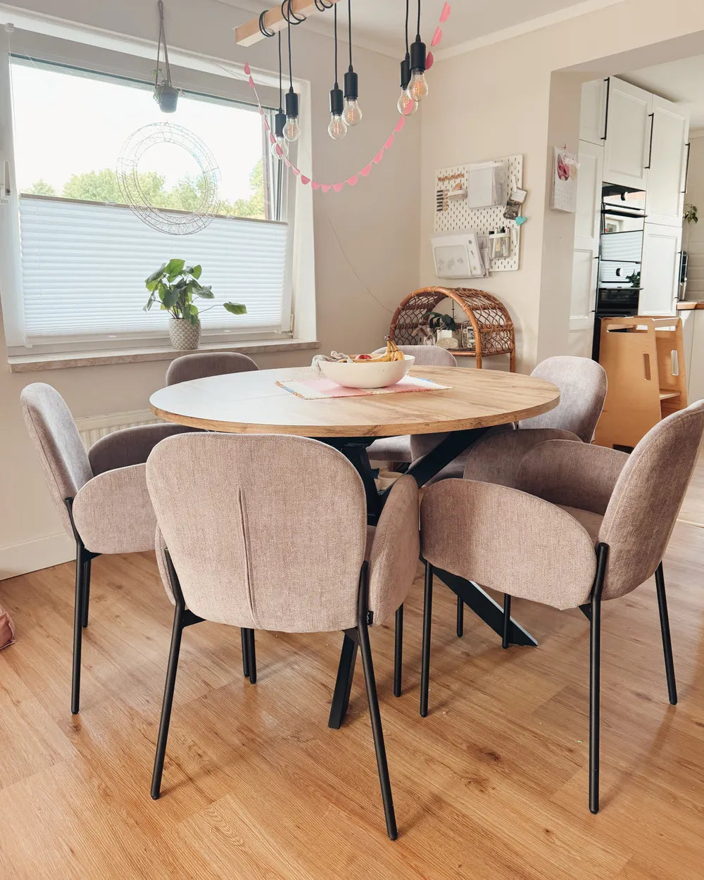 Dining area with a round wooden table and beige chairs in a well-lit room.