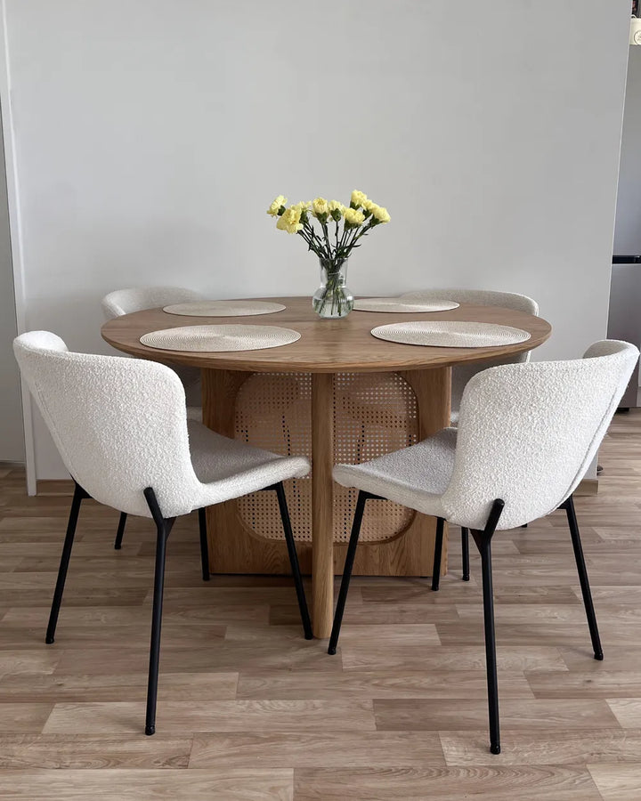 Round wooden dining table with four chairs in a modern room.