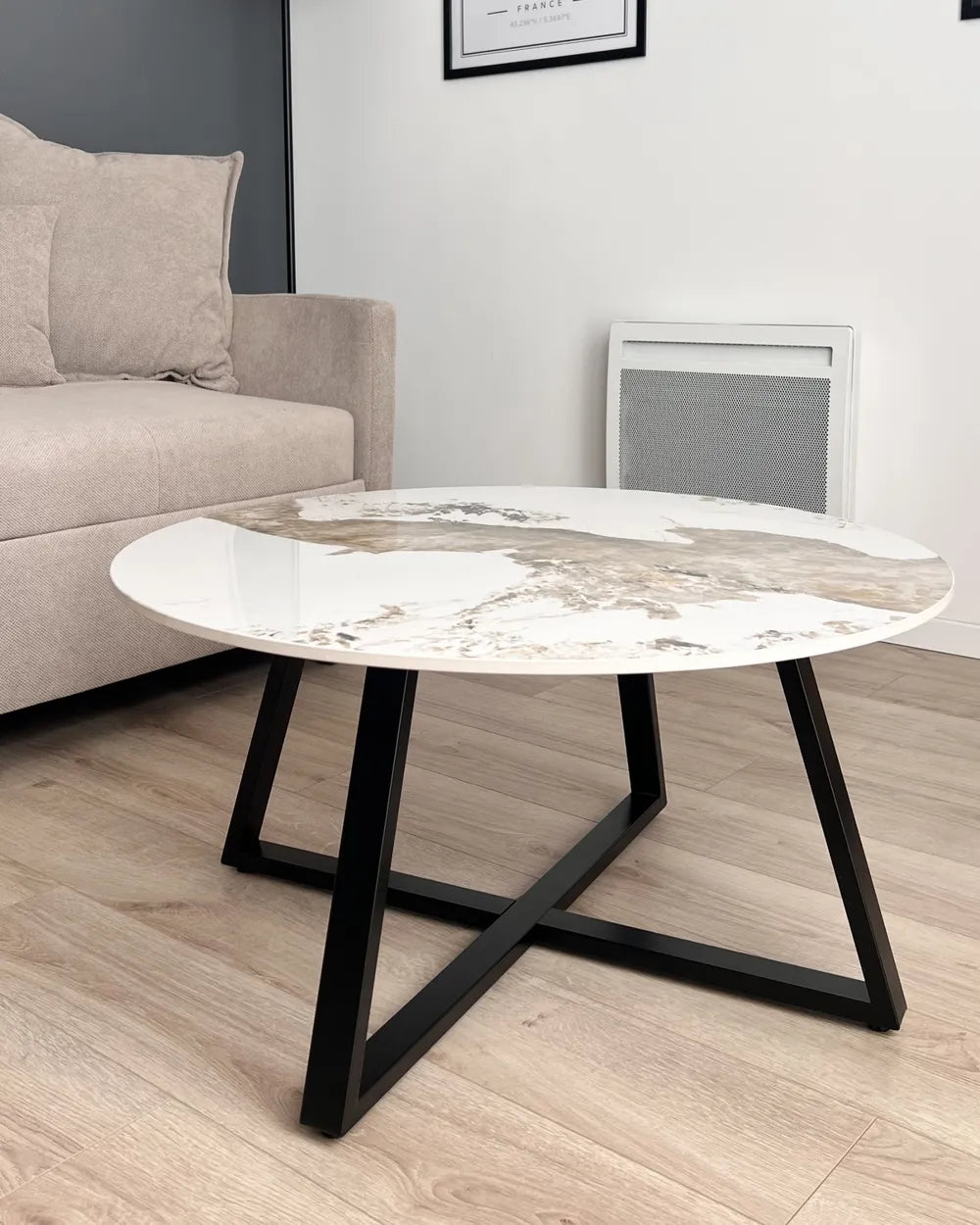 Round coffee table with marble-like top and black metal legs in a living room setting.