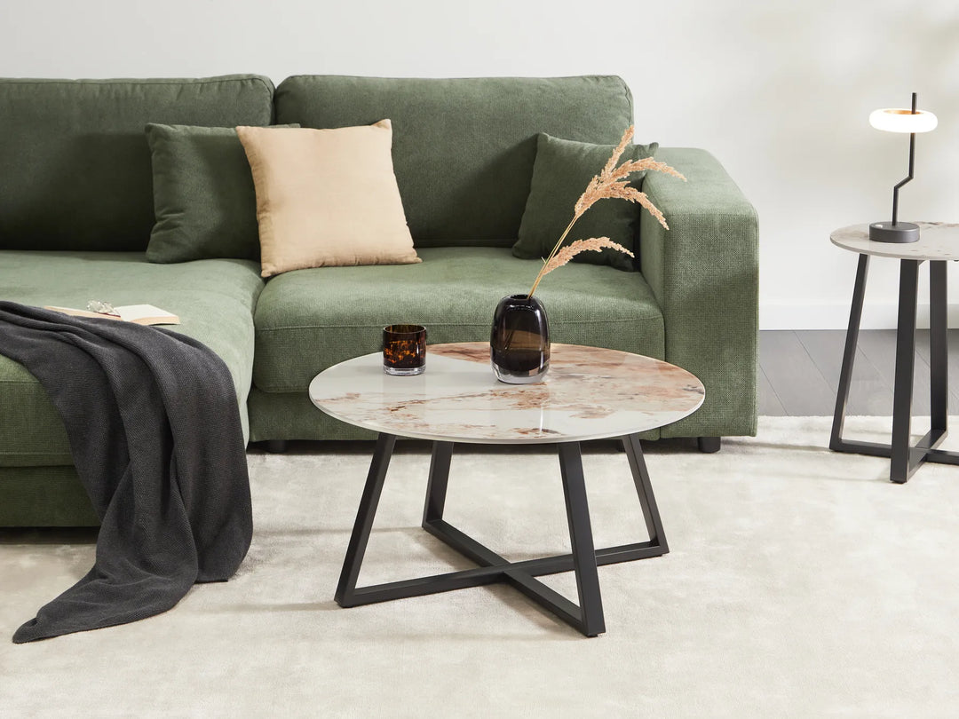 Green sofa with a beige pillow and a round coffee table in a living room setting.