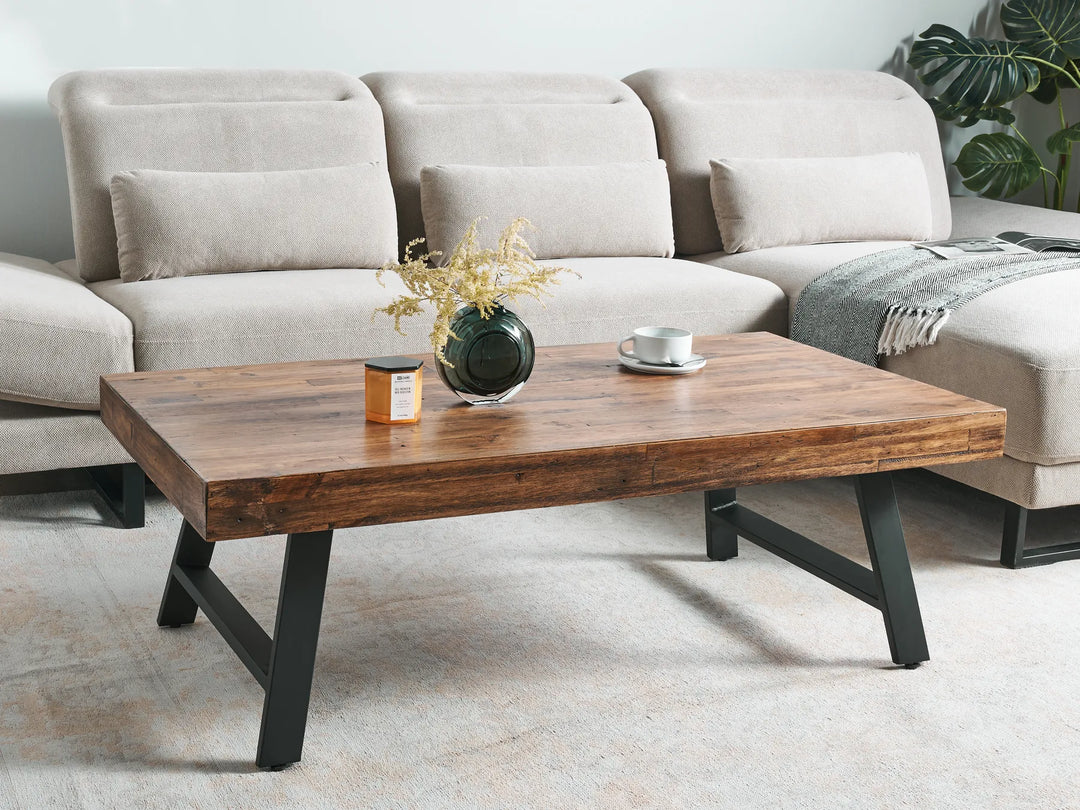 Wooden coffee table in front of a beige sectional sofa with decorative items on top.