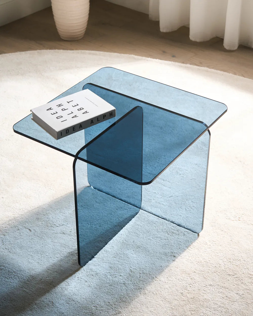 Blue glass coffee table with a book on a light-colored rug
