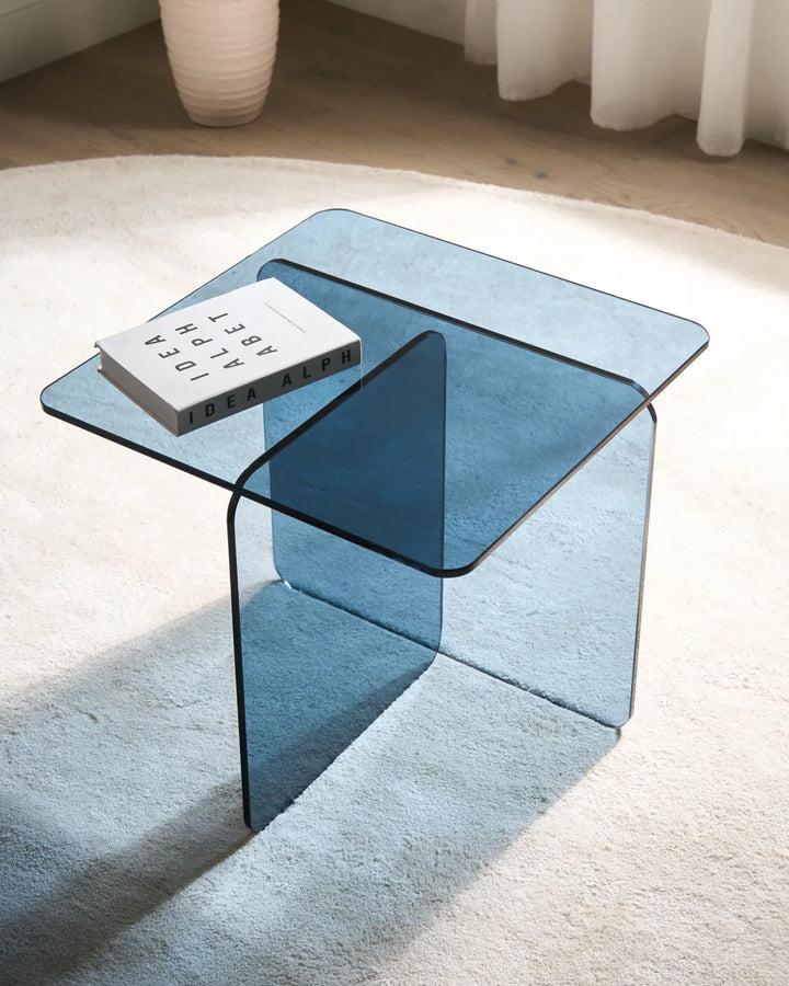 Blue glass coffee table with a book on a light-colored rug