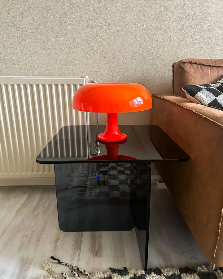 Orange lamp on a black glass table next to a brown sofa with a checkered pillow.