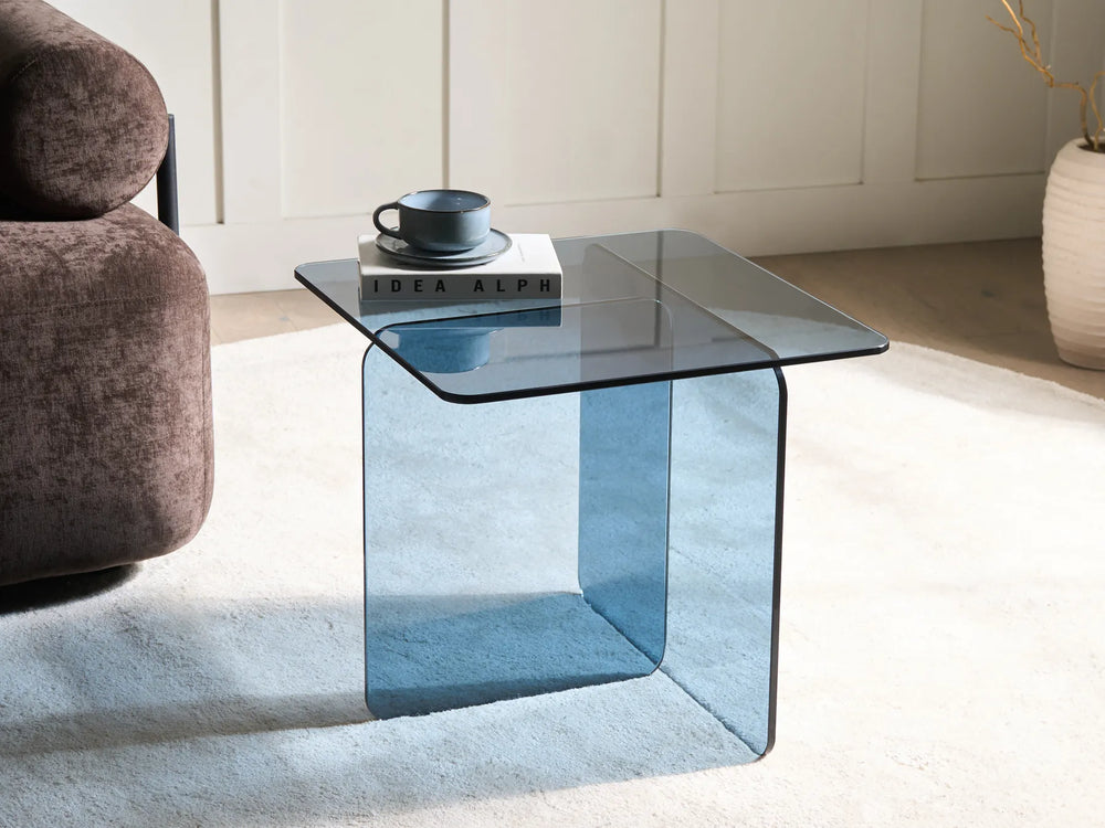 Blue glass side table with a book and mug in a living room setting