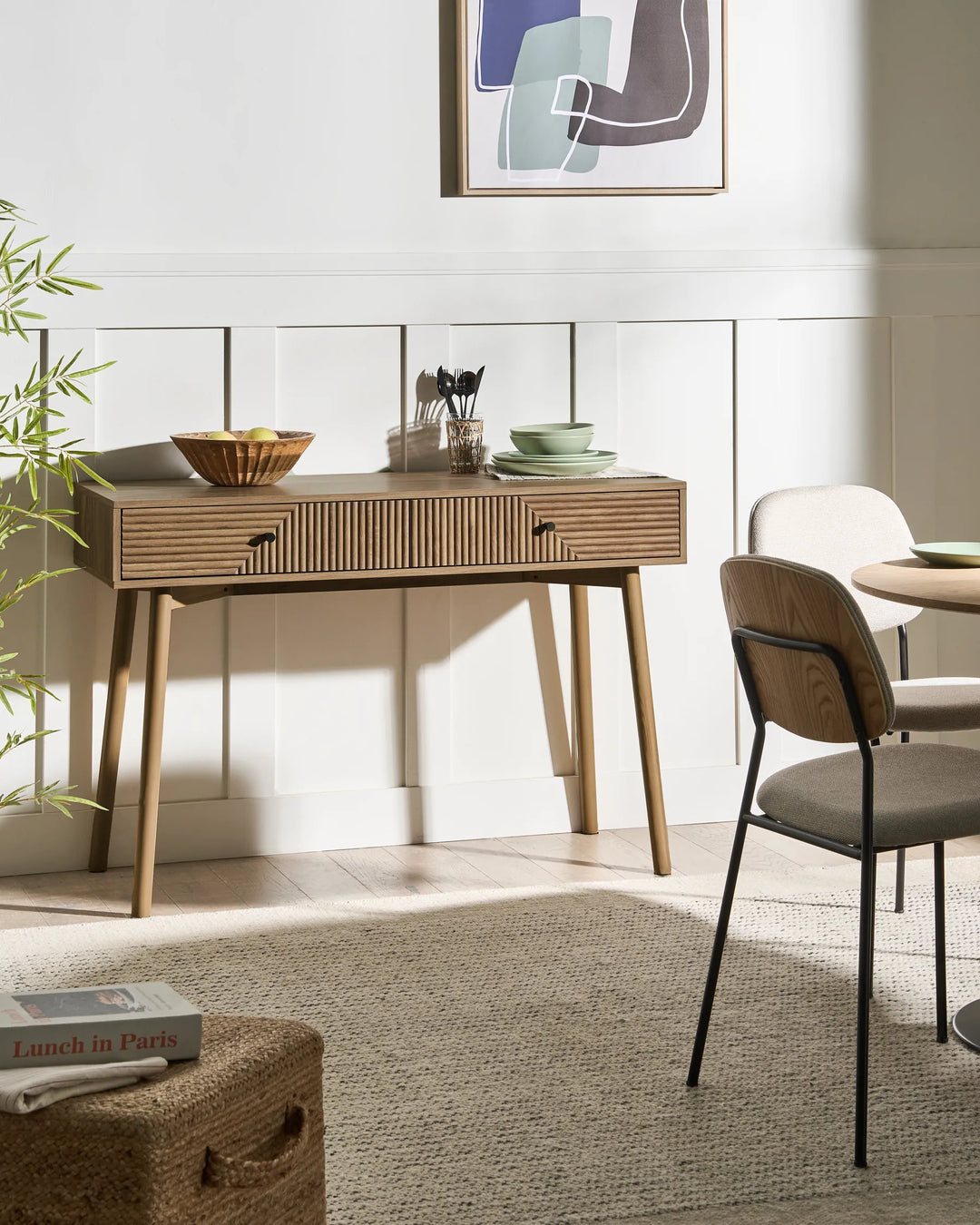 Wooden desk with a chair in a room with a mirror and abstract art on the wall.