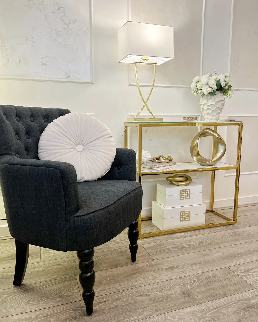 Gray armchair with a white cushion next to a gold side table with decorative items in a room.