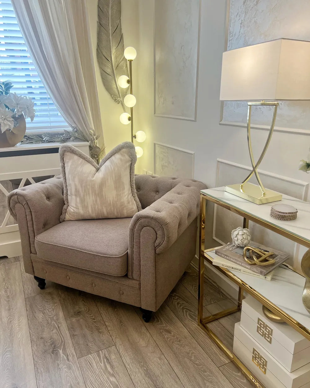 Beige armchair with decorative pillows in a stylish room with a lamp and side table.