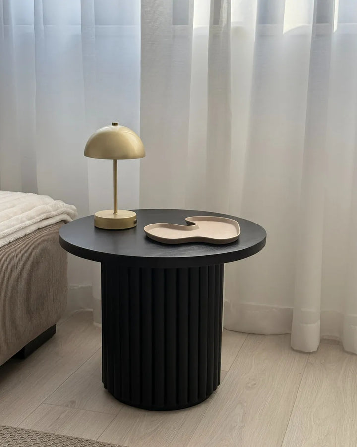 Black side table with a gold lamp and decorative plate against a neutral background