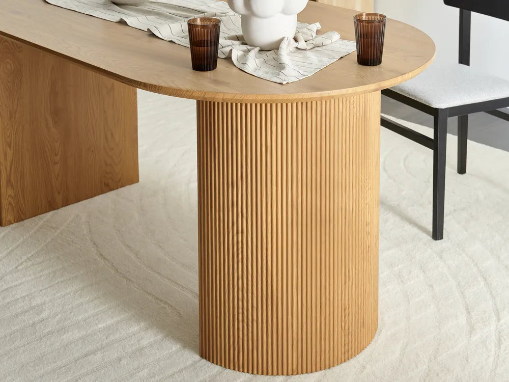 Wooden dining table with a textured cylindrical base on a light-colored floor.