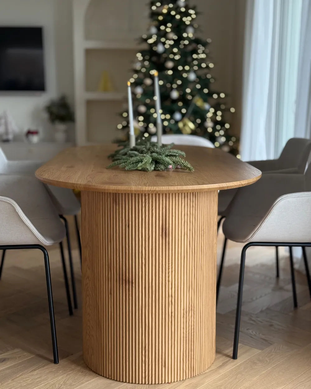 Wooden dining table with decorative candles and greenery in a living room with a Christmas tree.
