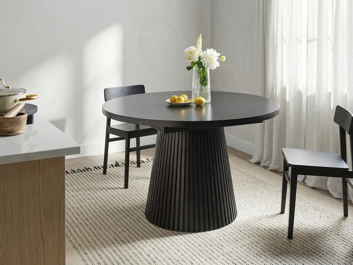 Dining room with a black round table and chairs, featuring a vase of flowers.